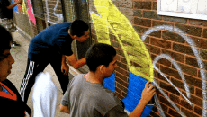 Imago Dei youth write the name of the program in graffiti as part of a mural covering existing graffiti at 27th Street and Ridgeway Avenue in Little Village.